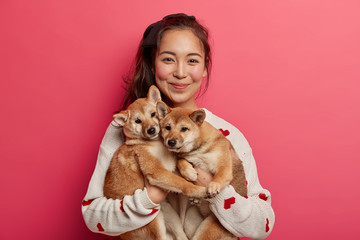Happy korean female dog owner shows her family members, stands with two adorable pedigree puppies,...