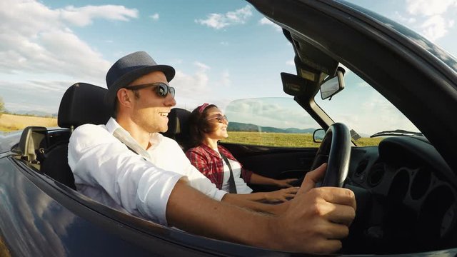 4K footage of young couple driving in right-hand wheel convertible at great speed. Clear warm day, wind blowing. Male driving.