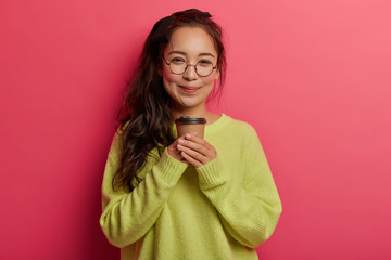 Portrait of attractive korean girl stands with takeaway coffee, enjoys caffeine beverage, looks...