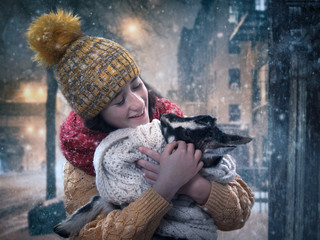 A girl with a newborn baby goat in her arms. Winter, snow
