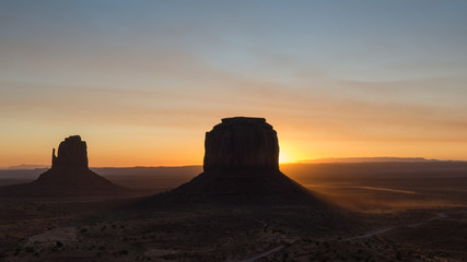 Fototapeta na wymiar Sun rising behind the Merrik Butte and the Mitten Butte in Monument Valley