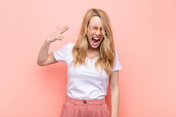 young pretty blonde woman looking unhappy and stressed, suicide gesture making gun sign with hand,...