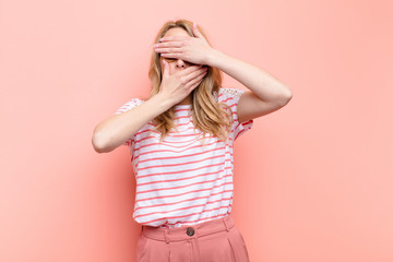 young pretty blonde woman covering face with both hands saying no to the camera! refusing pictures...
