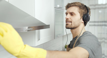 Closeup of young lad with beard in gloves wiping a kitchen hood