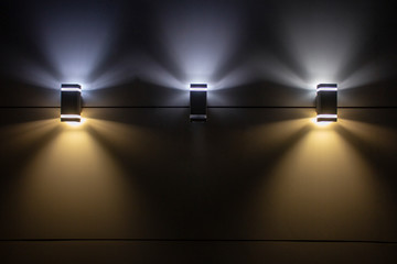 three lamps on the wall shining at night. - Powered by Adobe