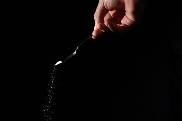 A male hand holds a small spoon from which white matter is poured out in total darkness under...
