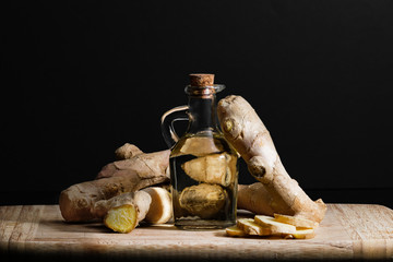 Ginger oil bottle with ginger roots and slices on wooden cutting board. Healthy eating concept.
