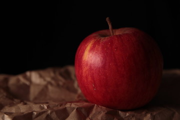 Ripe red apple on kraft paper and dark background under studio lighting