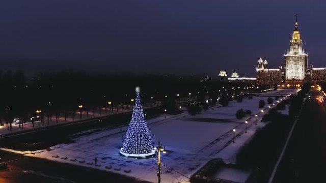 Glowing in the night the main building of Moscow State University (MGU) in the New Year and a luminous by garlands large Christmas tree nearby. Copter ( drone ) shooting