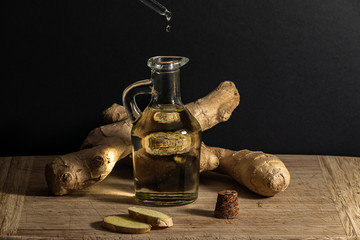 Ginger oil bottle with pipette and oil drop, ginger roots and slices on wooden cutting board....
