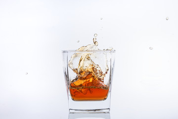 Alcohol in the glass. Whiskey and ice. Rum with ice. Brown brandy with splashes. Ice cube falls into a glass with splashes