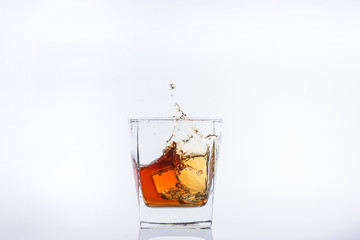 Whiskey and ice. Rum with ice. Brown brandy with splashes. Ice cube falls into a glass with splashes