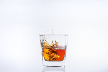 Alcohol in the glass. Whiskey and ice. Rum with ice. Brown brandy with splashes. Ice cube falls into a glass with splashes