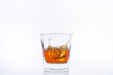 Alcohol in the glass. Whiskey and ice. Rum with ice. Brown brandy with splashes. Ice cube falls into a glass with splashes