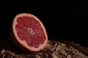 Half of grapefruit on kraft paper and dark background under studio lighting