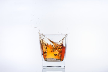 Whiskey and ice. Rum with ice. Brown brandy with splashes. Ice cube falls into a glass with splashes