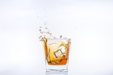 Whiskey and ice. Rum with ice. Brown brandy with splashes. Ice cube falls into a glass with splashes