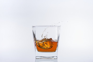 Whiskey and ice. Rum with ice. Brown brandy with splashes. Ice cube falls into a glass with splashes