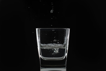 Drops of water or alcohol fall into a glass glass on a black background. Close-up photo
