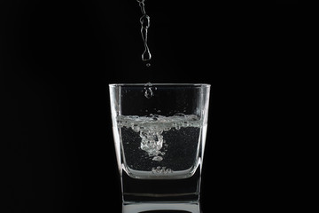Water or alcohol falls in a glass on a black background. Close-up photo