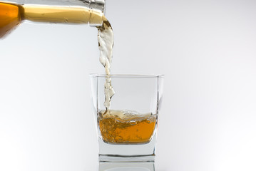 Whiskey being poured into a glass against white background