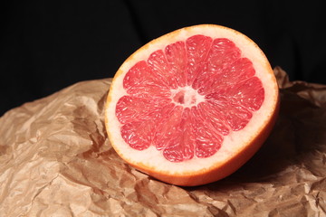 Half of grapefruit on kraft paper and dark background under studio lighting