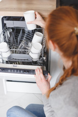 Housework: young woman putting dishes in the dishwasher