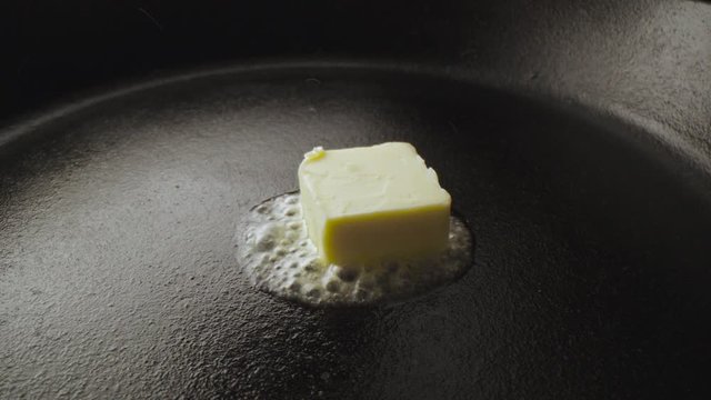 Close up of dropping butter into a cast iron pan, with sound
