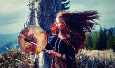 beautiful shamanic girl playing on shaman frame drum in the nature.