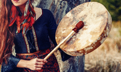 beautiful shamanic girl playing on shaman frame drum in the nature.