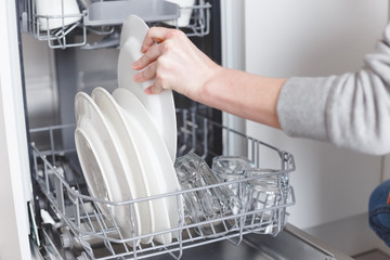 Housework: young woman putting dishes in the dishwasher