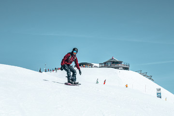 Freeride snowboarder rolls on a snow-covered slope leaving behind a snow powder against the blue sky