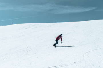 Freeride snowboarder rolls on a snow-covered slope leaving behind a snow powder against the blue sky