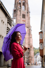 Calm dreaming girl having a walk in town while raining. Attracting caucasian girl with purple umbrella enjoying warm summer rain