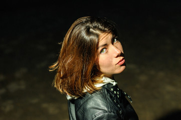 cute young brunette girl in a black jacket looks over her shoulder in the dark