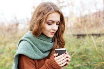 Young adult woman in a brown knitted sweater. Coffee in a plastic glass. The concept of a lifestyle, autumn, art, cosmetics and care. Nature. The concept of a lifestyle, autumn, cosmetics and care.