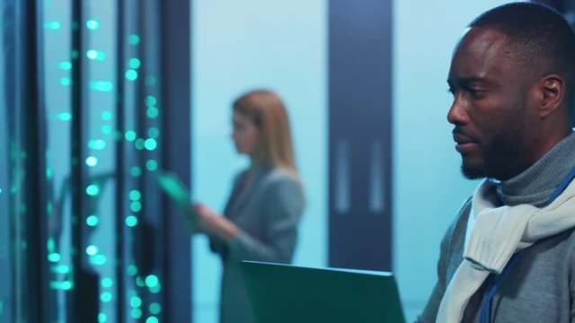Afro-american IT administrator diagnosing rack servers in cyber security. Black technician conferring with woman head engineer solving tech issues coworking in database.