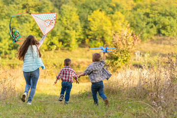 Happy family of young mother and its kids launch a kite on nature at sunset. Family holidays