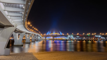 Fototapeta na wymiar Russia, Saint Petersburg, November 2019:The new Zenit arena stadium, where the 2018 FIFA world Cup was held. Night view from under the pedestrian bridge intertwined with the bridges of the ZSD highway