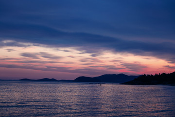 Rocky island silhouette in the sea during purple sunset.