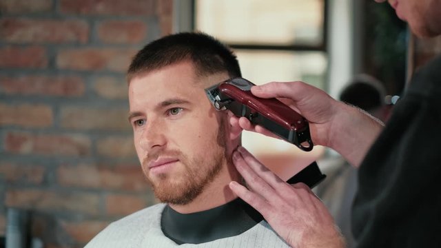 Male haircut with electric razor. Close up of man hair cut. Male hands barber shaving man with electric razor in barbershop. Barber cutting hair with hair trimmer.