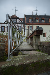 Fototapeta na wymiar Small footbridge leading to watermill near river Mumling in town Erbach, Odenwald, Hesse, Germany.