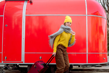 girl runs with a red suitcase on a red background. Large retro vintage van. Old car. Traveling in the winter. Girl in a yellow bright hat and knitted sweater. Travel concept.