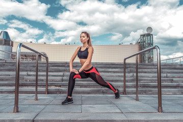 Athletic girl doing stretching before jogging, summer in city, lifestyle motivation, exercising and training on the street. Cloud stair background. Sportswear Leggings Top.