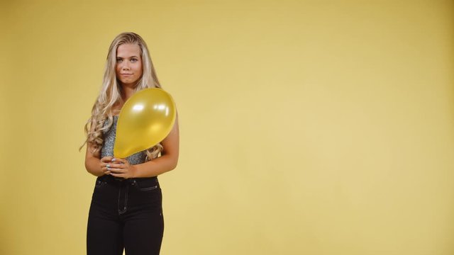 Female Model in Silver Tank Top Holding a Ballon Against a Yellow Background