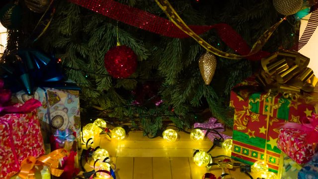 Place for a Gift under the Christmas Tree. The camera slowly goes down under the decorated Christmas tree under which there are gifts in colorful boxes. In the middle of the frame there is an empty pl