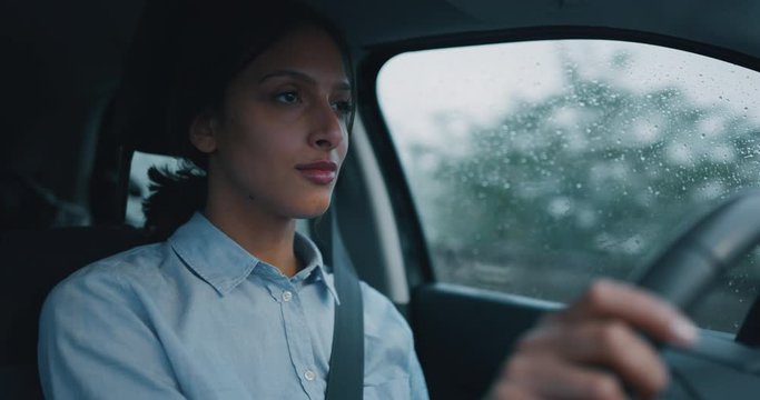 An young businesswoman is driving a modern car in a center of the city by day while is raining outside.