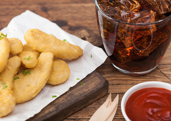 Buttered chicken nuggets on chopping board with glass of cola and ketchup on wooden background.
