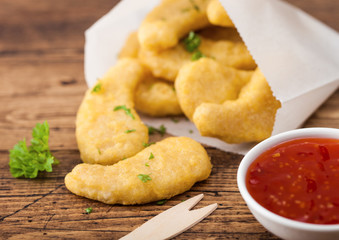Buttered chicken nuggets in paper bag with wooden forks and ketchup on wooden background.