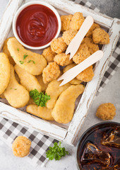 Buttered chicken nuggets and popcorn bites in white vintage wooden box with ketchup and glass of cola on light background.